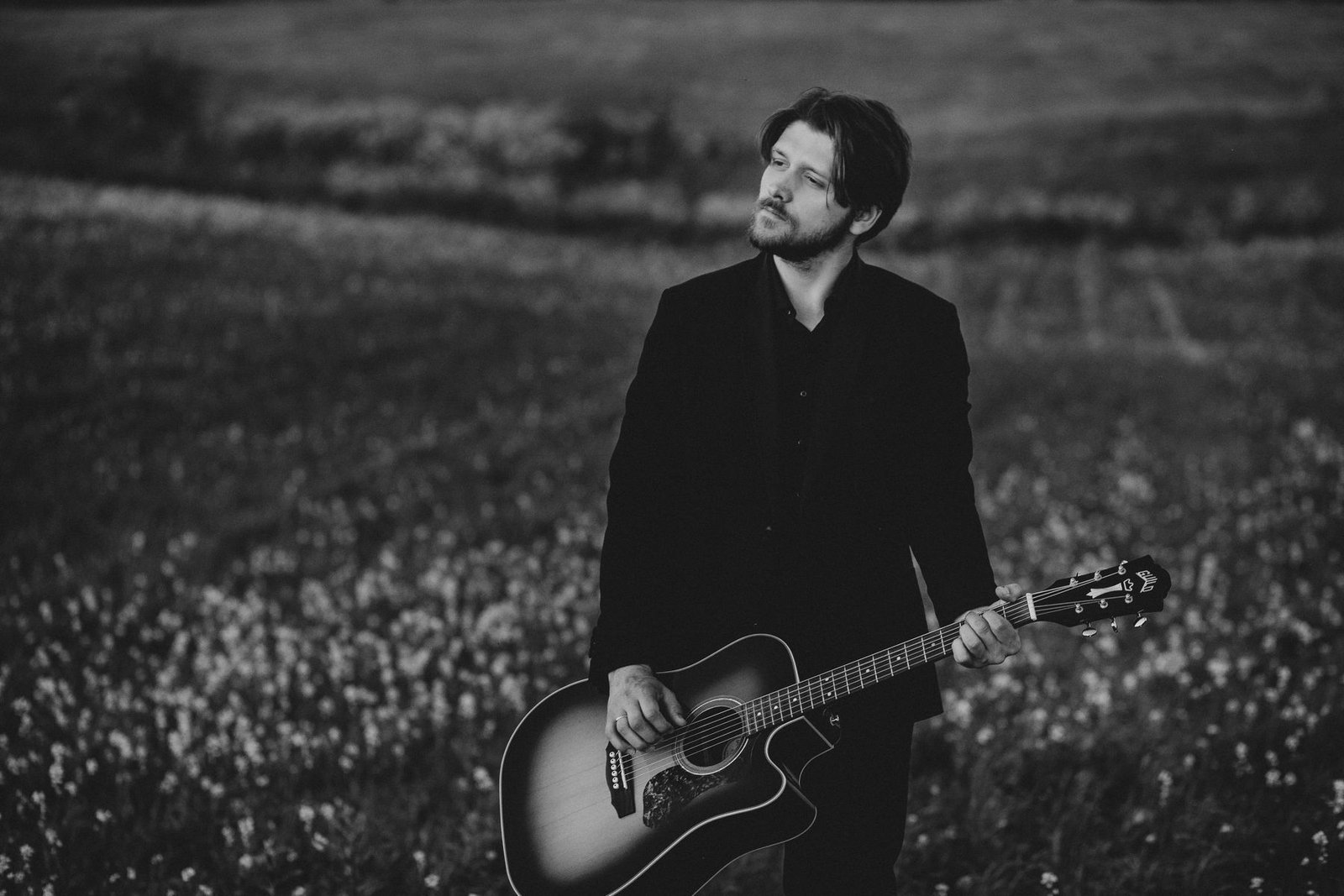 Justinas Stanislovaitis with a guitar in a field, black and white