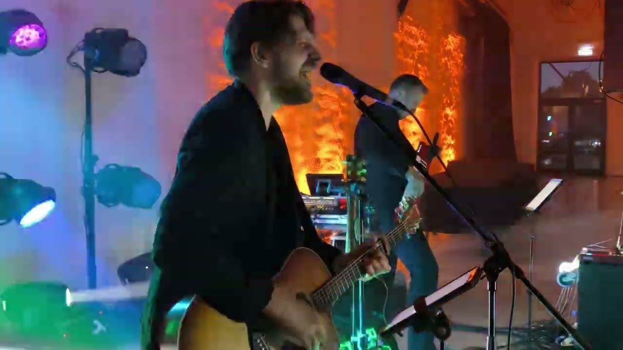 Justinas Stanislovaitis ir grupė koncertuoja scenoje su mėlynais šviesų spinduliais